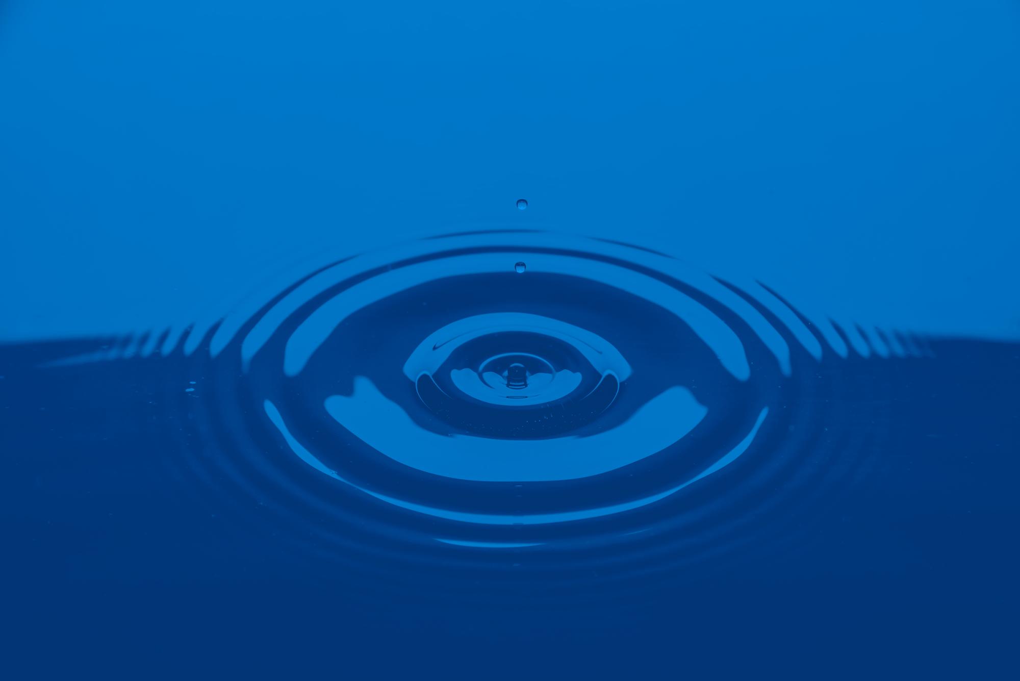 A drop falls onto a smooth water surface causing concentric rings  to move outward