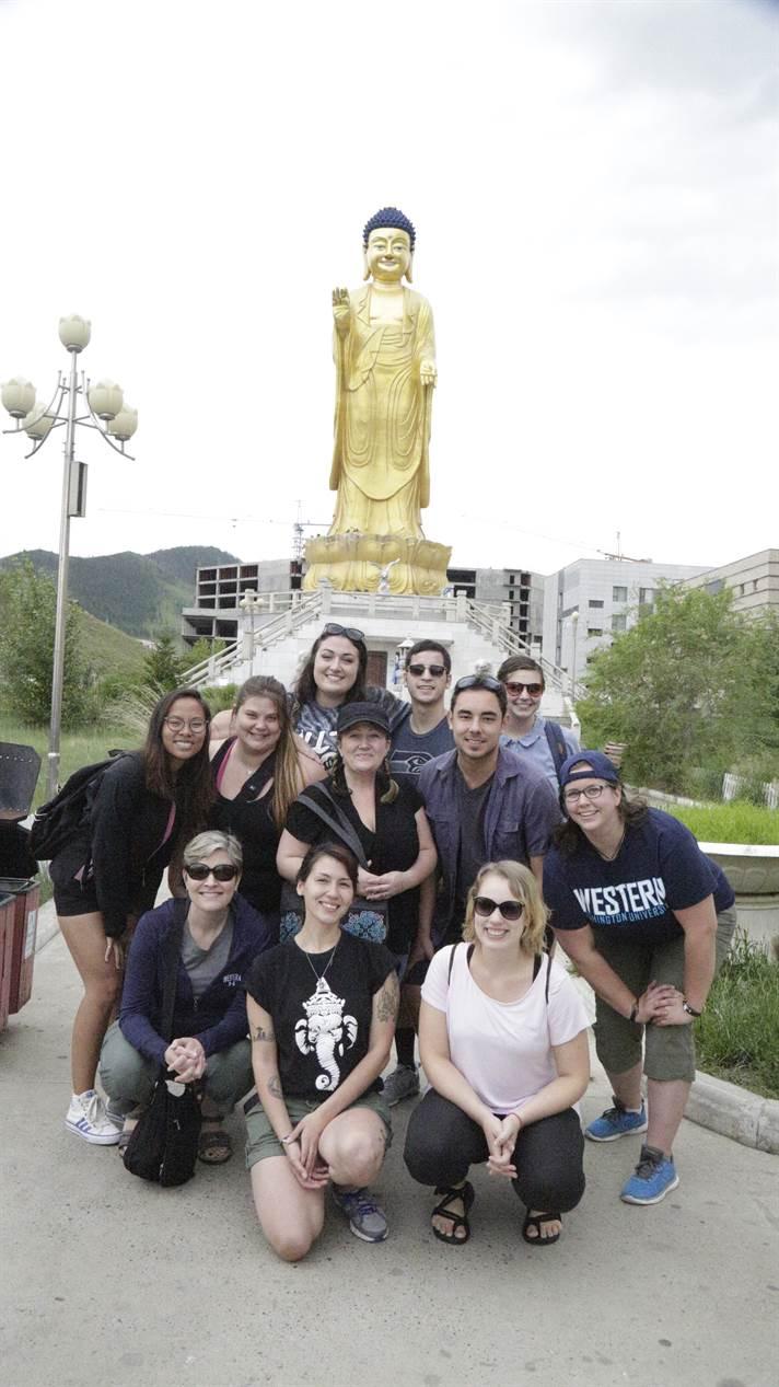 Group of students stand in front of a gold Buddha statue