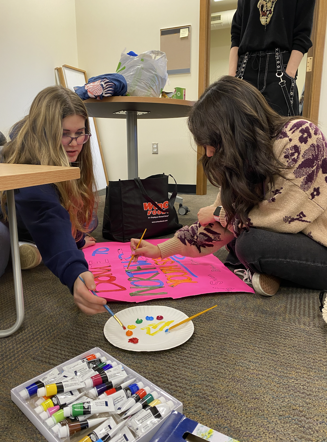 Two students in a room on the floor making posters for trans youth advocacy 