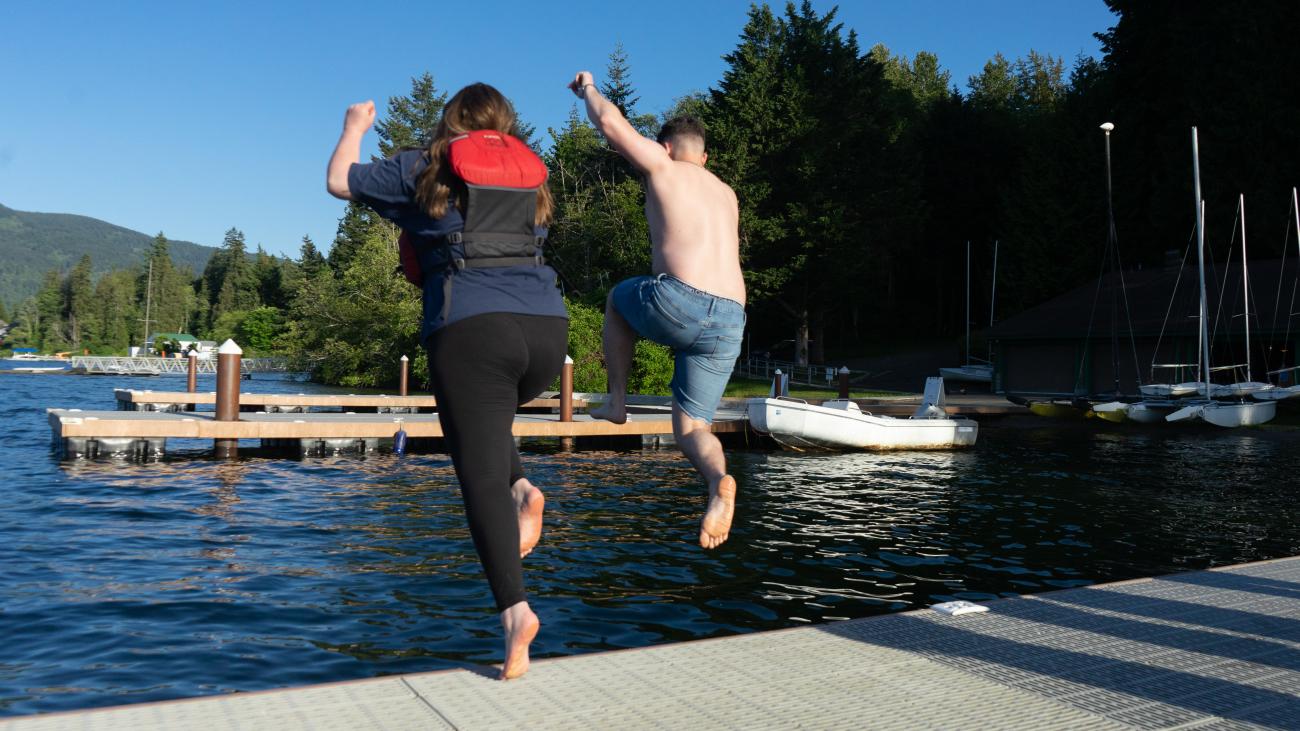 two people facing away from the camera jumping off a dock into a lake