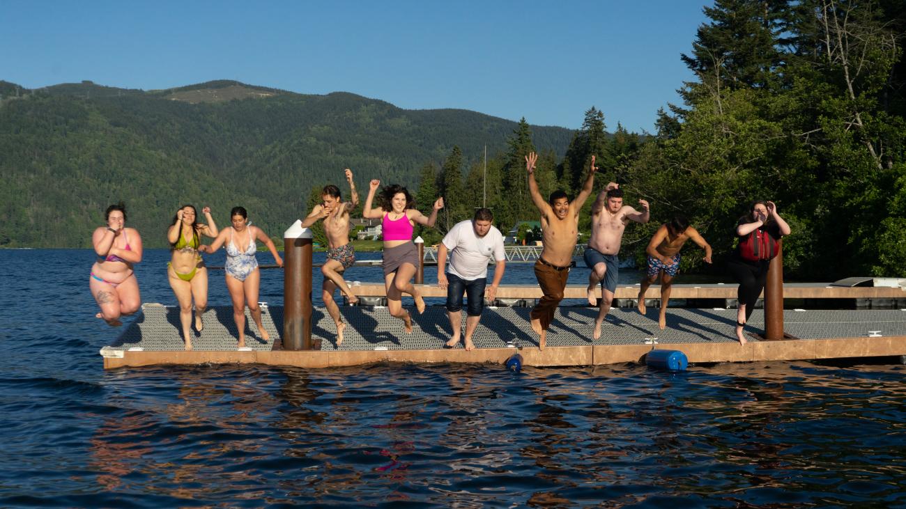 student emplyees in swimsuits jumping off the dock into the water