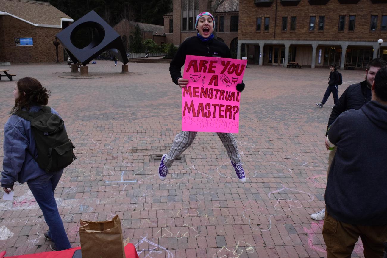 person jumping, withan open mouthed smile, holding a poster that says "are you a menstrual master?"