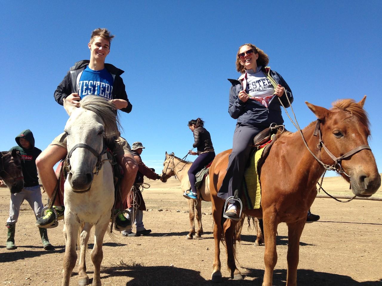 two people on horseback smiling at the camera and holding open their jackets to show a WWU t-shirt